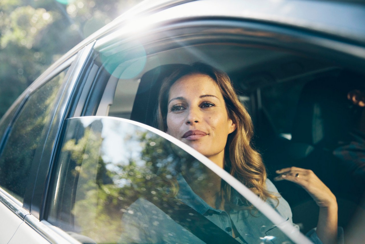 Kvinde i bil med åbent vindue i solskin