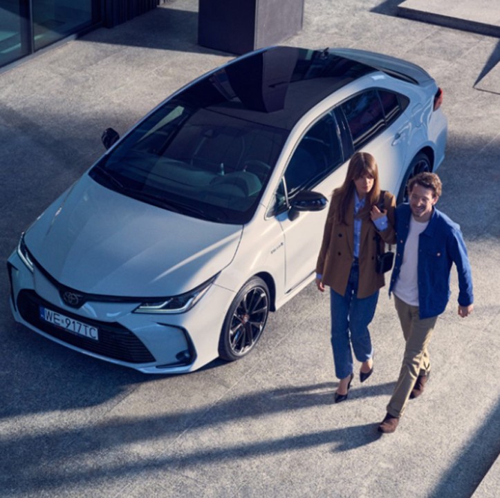Kobieta i mężczyzna przechodzą obok Toyoty Corolla
